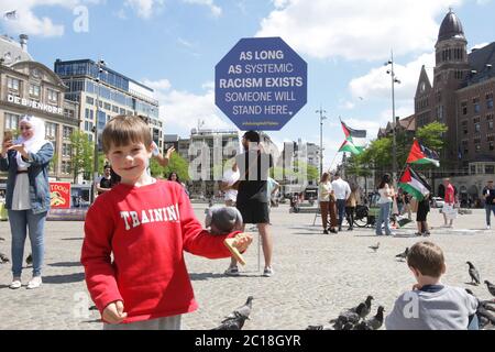 Zwei junge Jungen füttern Tauben und ein Protestor hält ein Plakat mit dem Zeichen ‘solange systemischer Rassismus existiert, wird jemand hier stehen’ während Anti-rac Stockfoto