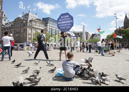 Ein Junge füttert Tauben und ein Protestler hält ein Plakat mit dem Zeichen ‘solange systemischer Rassismus existiert, wird jemand hier stehen’ während des Antirassismus Stockfoto