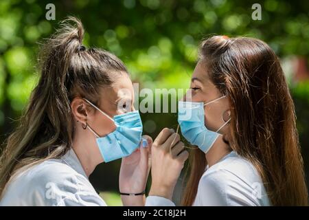 Nahaufnahme von zwei jungen Frauen, die chirurgische Masken tragen und sich gegenseitig anlächeln, auf einem unfokussierten Hintergrund. Neues Lifestyle- und Sicherheitskonzept. Stockfoto