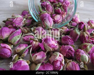 Rosa getrocknete Rosenblüten (Kräutertee) in Glasflasche auf Holzhintergrund.. Reduzierte Symptome von Depressionen, beruhigte Nerven, erhöhte Durchblutung und impro Stockfoto