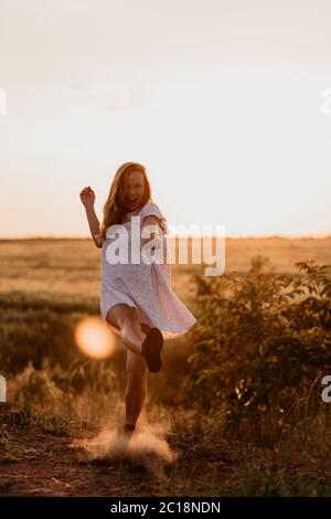 Junge schöne Frau, die mit dem Fuß Staub macht und an einem sonnigen Sommertag im Weizenorangenfeld schreit. Verrückt. Sich frei und glücklich fühlen Stockfoto