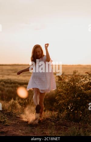 Junge schöne Frau, die mit dem Fuß Staub macht und an einem sonnigen Sommertag im Weizenorangenfeld schreit. Verrückt. Sich frei und glücklich fühlen Stockfoto