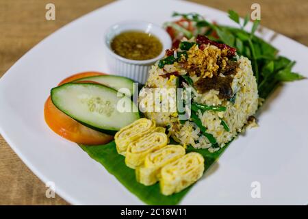 Würziger gebratener Reis mit Rindfleisch und Wasser Spinat mit geschnittenem Eierrollen und garnieren mit Gurke und Tomaten. Stockfoto