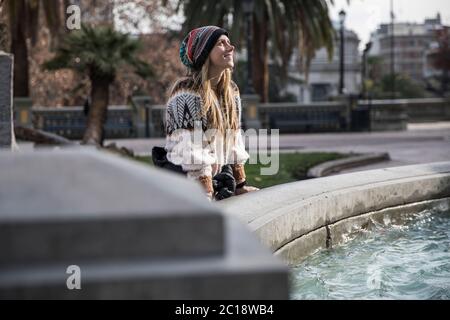 Schöne junge blonde Frau in der Nähe eines Wasserbrunnens Blick bis lächelnd Stockfoto