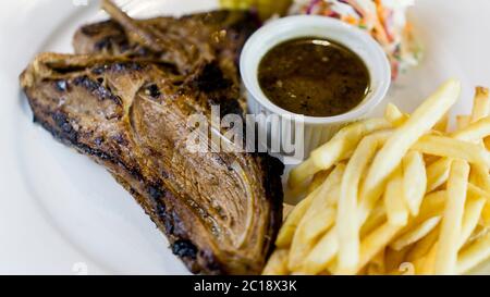 Saftiges Lammkotelett Grill zur Perfektion mit Grillsauce, pommes frites, Mais und Krautsalat als Beilagen. Stockfoto