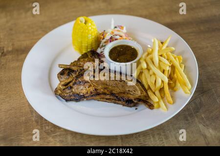 Saftiges Lammkotelett Grill zur Perfektion mit Grillsauce, pommes frites, Mais und Krautsalat als Beilagen. Stockfoto