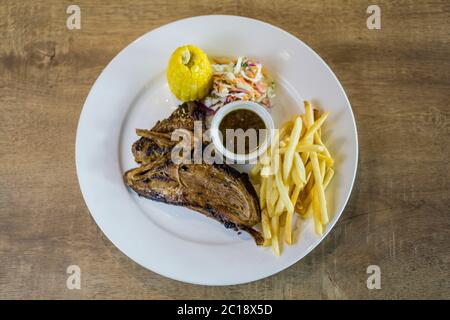 Saftiges Lammkotelett Grill zur Perfektion mit Grillsauce, pommes frites, Mais und Krautsalat als Beilagen. Stockfoto