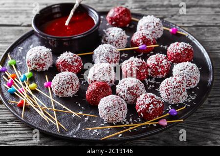 Kalorienarmer Nachtisch: beerenklischeebällchen mit Kokosnuss, die mit Erdnussbutter und einer frischen Mischung aus Himbeeren, Brombeeren, Blaubeeren auf einem B gemischt ist Stockfoto
