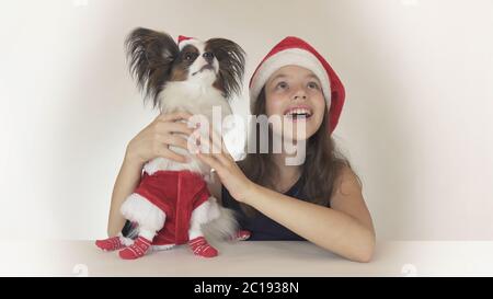 Schöne Teenager-Mädchen und Hund Continental Toy Spaniel Papillon in Santa Claus Kostüme freudig suchen und lachen auf whi Stockfoto
