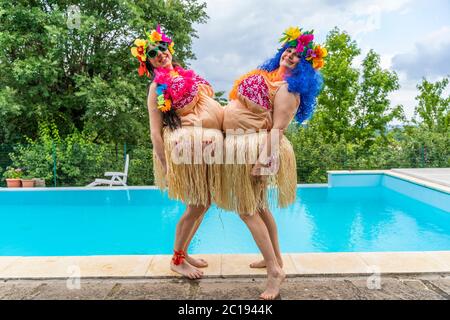 Zwei Freundinnen in fetten Hawaii Kostümen haben Spaß vor dem Pool Stockfoto