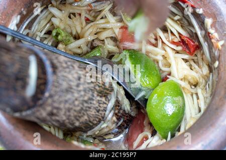 Zubereitung des beliebten Thai Papaya Salats, die frischen Zutaten werden mit Stößel in Mörser zerschlagen, Nahaufnahme. Stockfoto