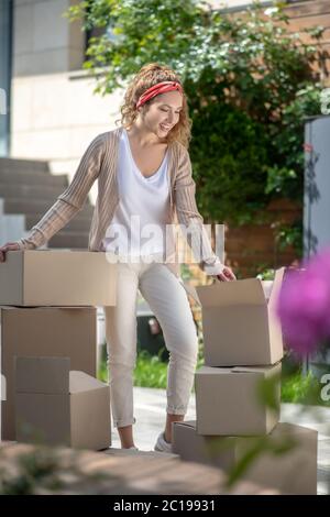 Junge hübsche Frau, die neben den Kartons steht und wartet Stockfoto