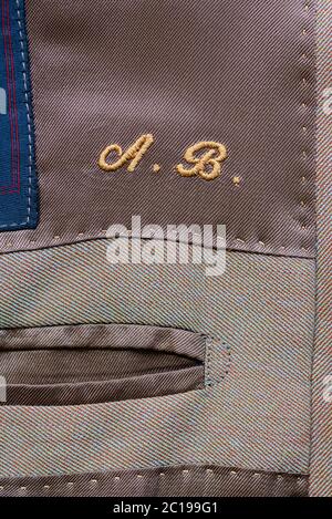 Initialen bestickt in einem maßgeschneiderten Kleidungsstück in gelbem Faden über einer Innentasche in Nahaufnahme auf dem Textil Stockfoto
