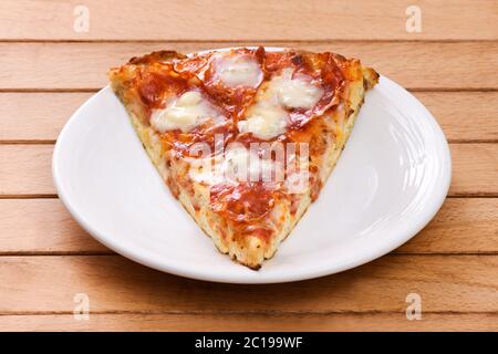Ein Stück italienische Salami-Pizza mit würzigem Gorgonzola-Käse auf einem weißen Teller auf einem Holztisch serviert Stockfoto