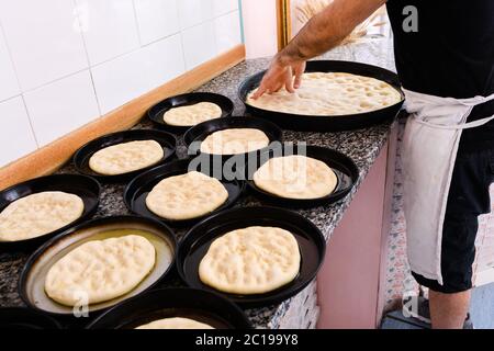 Koch streckt während der Zubereitung Portionen Pizzateig in einzelnen Backblechen in einer Pizzeria-Küche Stockfoto