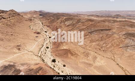 Luftaufnahme von wadi gevanim mit Akazien übersät Blick nach Westen mit der Wüste Stadt mitzpe ramon auf der Klippe im rechten Hintergrund weit Stockfoto