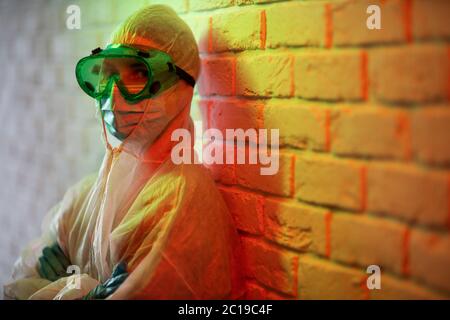 Junger Arzt in Schutzanzug und Brille auf dem Hintergrund Ziegelwand in roter Zone Stockfoto