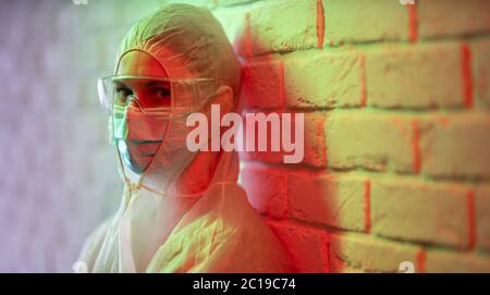 Arzt im Schutzanzug auf dem Hintergrund der Ziegelwand in der roten Zone. Stockfoto