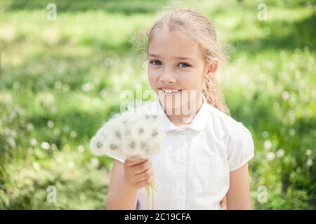 Ein Mädchen im Vorschulalter oder Grundschulalter mit Löwenzahn in der Hand auf einer Sommerwiese. Stockfoto