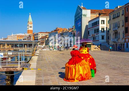 Hölzerne Piers, Karneval verkleidete Frau an der dennoch ruhigen Küstenstraße ohne Massen von Touristen und die schönen historischen Gebäude am Meer in Venedig Stockfoto