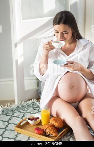 Schwangere Frau mit Frühstück mit Kaffee, Orangensaft, croisan und Haferflocken. Stockfoto