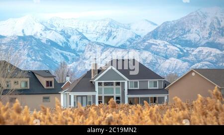 Panorama Frame Häuser und atemberaubende schneebedeckten Berg mit verschwommenen braunen Gräsern im Vordergrund Stockfoto