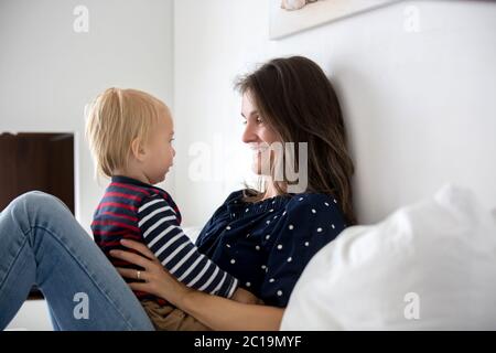 Junge Mutter und ihr niedlicher kleiner Sohn umarmen zu Hause in sonnigen Schlafzimmer Stockfoto