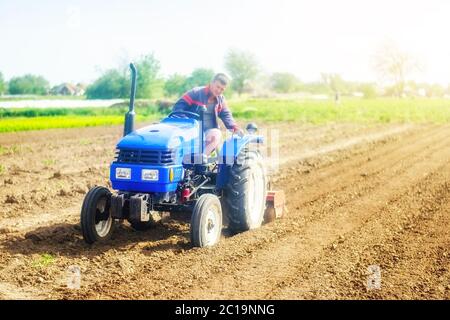 Ein Bauer auf einem Traktor bewirtschaftet ein Ackerfeld. Landwirtschaft, Anbau von Bio-Lebensmittel Gemüse. Bodenfräsen, Zerbröckeln und Mischen. Lockern der Oberfläche Stockfoto