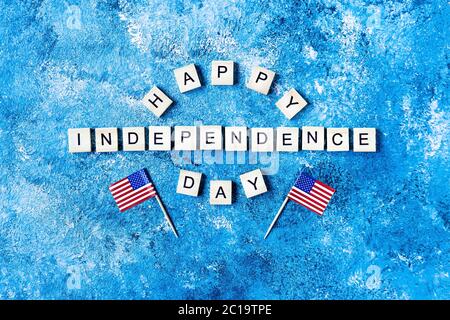 Inschrift des Unabhängigkeitstages in Holzbuchstaben auf blauem Hintergrund. Alles Gute Zum Unabhängigkeitstag. Der 4. Juli. USA Unabhängigkeitstag. Amerikanische Flaggen. Co Stockfoto