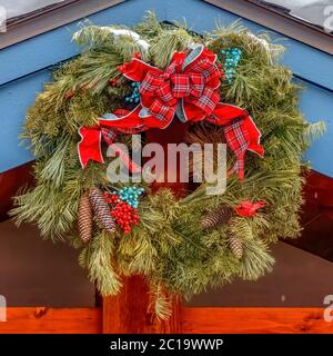 Quadratischer Weihnachtskranz aus immergrünen Blättern gegen schneebedecktes Dach Stockfoto