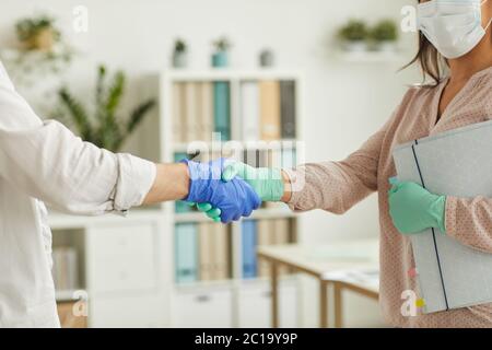 Nahaufnahme von zwei Personen, die Handschuhe tragen und sich bei der Arbeit im Büro die Hände schütteln, Platz kopieren Stockfoto