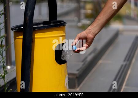 Selektive Konzentration auf das Ablegen einer leeren Plastikflasche in den gelben Abfalleimer. Stockfoto