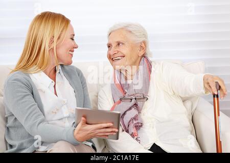 Lächelnde Erwachsene Frau, die einem älteren Bürger einen Tablet-Computer zeigt Stockfoto