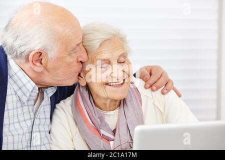 Happy Senior küsst seine lächelnde Frau auf die Wange am Computer Stockfoto