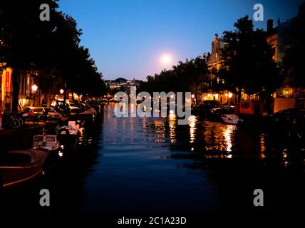 Nachtansicht zum Amsterdamer Kanal mit Mond, Niederlande Stockfoto