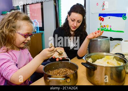 Mutter und ihr Teigschaber bereiten zusammen gefüllte Sauerkrautkohlrollen aus Blatt mit Hackfleisch und Reis zu. Stockfoto