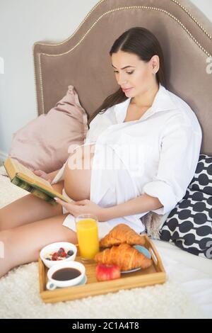 Schwangere Frau mit Frühstück mit Kaffee, Orangensaft, croisan und Haferflocken. Stockfoto