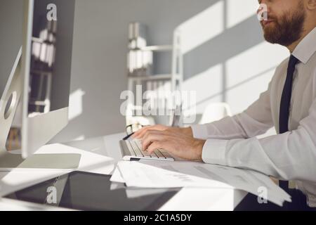 Online arbeiten. Serious beschäftigt Geschäftsmann liest Arbeitsdokumente sitzen an einem Tisch mit einem Computer im Büro. Stockfoto