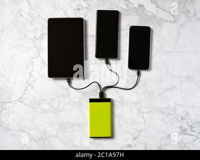 Tech Device Charge Sharing: Zwei Mobiltelefone und Tablet Laden von einem Powerbank-Ladegerät. Flach liegend, Draufsicht auf Marmorhintergrund Stockfoto