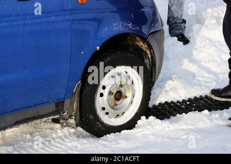 Schwarze Anti-Rutsch-Matte von einer rechteckigen Form wird unter dem Rad eines niedrig nivellierten Autos platziert, nachdem es in einer Schneeverwehung und s stecken Stockfoto