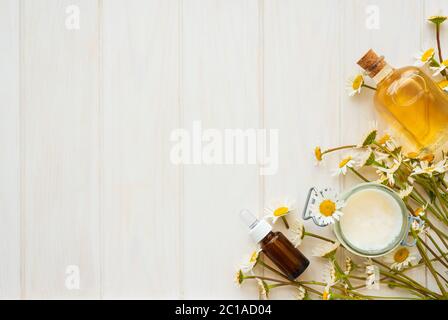 Kamillenblüten und kosmetische Flaschen ätherisches Öl und Extrakt auf weißem Holzhintergrund. Flaches Lay. Draufsicht. Kopierbereich Stockfoto