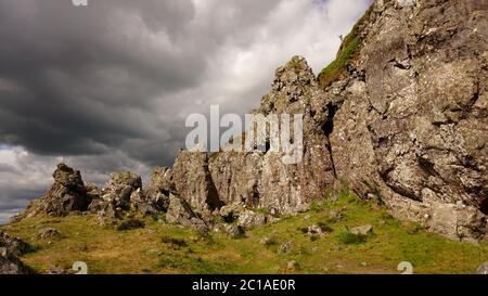 Felsbrocken vor launisch bewölktem Himmel. The Whangie in den Kilpatrick Hills, Schottland. Stockfoto