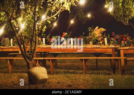 Bereit für ein rustikales Abendessen im Freien bei Nacht mit Weingläser, die Blumen und die Lampen Stockfoto