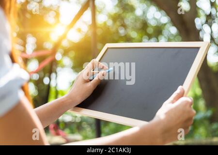 Die Hände verwenden die Kreide zum Zeichnen, das Balckboard in den Parks schreibendes. Bildung, Lernkonzept. Stockfoto