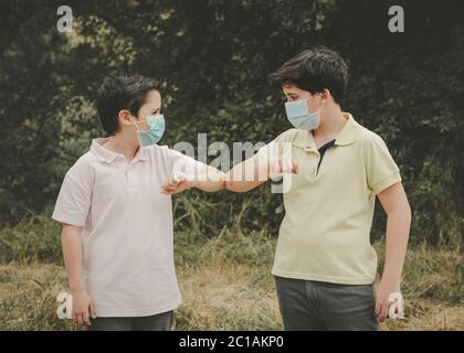Zwei Kinder mit medizinischer Maske Beulen Ellbogen, soziale Distanzierung Konzept im Freien Stockfoto