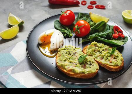 Gesundes Toast mit Avocado mexikanische Sauce Guacamole, gekochtes Ei, Kirschtomaten und Salat auf Beton Hintergrund. Frühstück Stockfoto