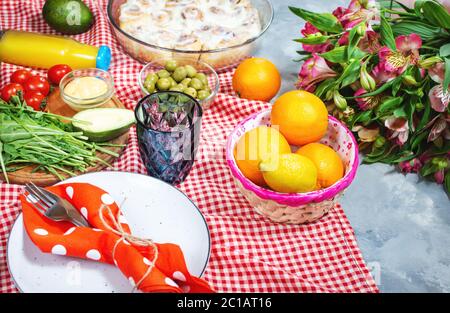 Hausgemachtes Picknick mit frischem Obst, Gemüse, Salat, Orangensaft, Blumen und Baguette auf rotem Karo. Schönes Stillleben. Stockfoto