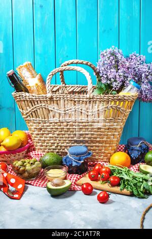 Hausgemachtes Picknick mit frischem Obst, Gemüse, Salat, Orangensaft, Blumen und Baguette im Weidenkorb. Schönes Stillleben. Stockfoto