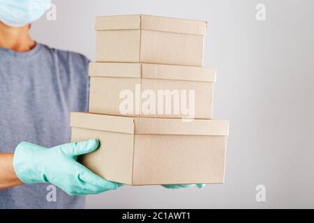 Der Kurier hält ein Paket von Kartons mit blauen Gummihandschuhen in der Hand. Stockfoto