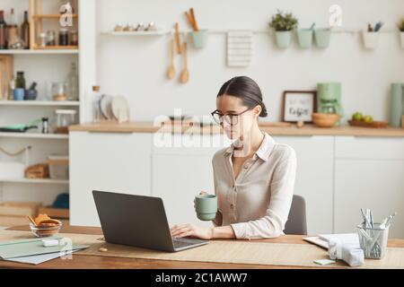 Porträt der eleganten Geschäftsfrau trinken Kaffee, während mit Laptop an gemütlichen Home Office-Arbeitsplatz, kopieren Raum Stockfoto